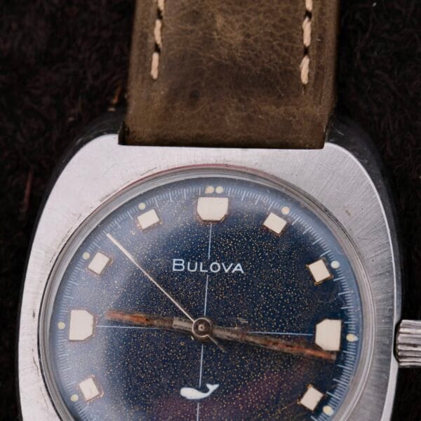 Close-up of a vintage Bulova Sea King Blue Cross Hair Dial watch featuring a blue speckled face, silver casing, and tan leather strap with white square hour markers and an arrow-shaped hour hand showing signs of aging.
