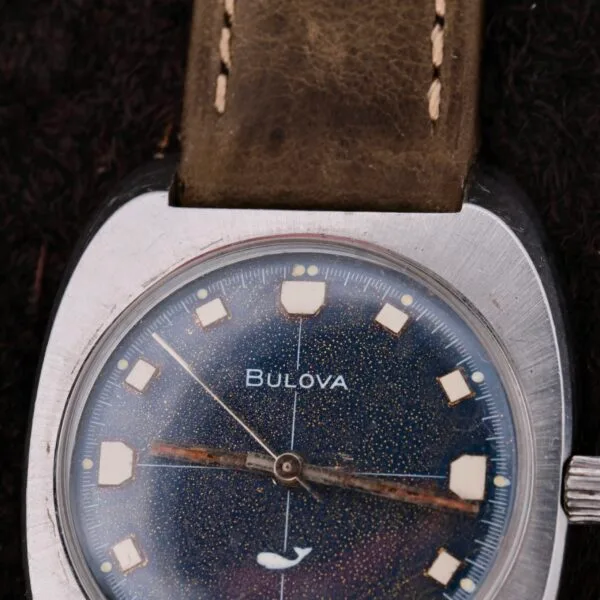 Close-up of a vintage Bulova Sea King Blue Cross Hair Dial watch featuring a blue speckled face, silver casing, and tan leather strap with white square hour markers and an arrow-shaped hour hand showing signs of aging.