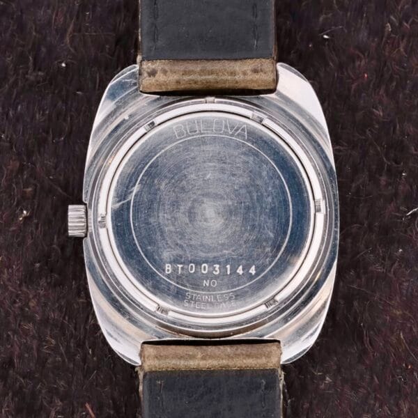 The back of a Bulova Sea King Blue Cross Hair Dial watch features a silver case and black leather strap. Engraved with Bulova BT003144, No, Stainless Steel, N4, it rests elegantly on a dark textured surface.