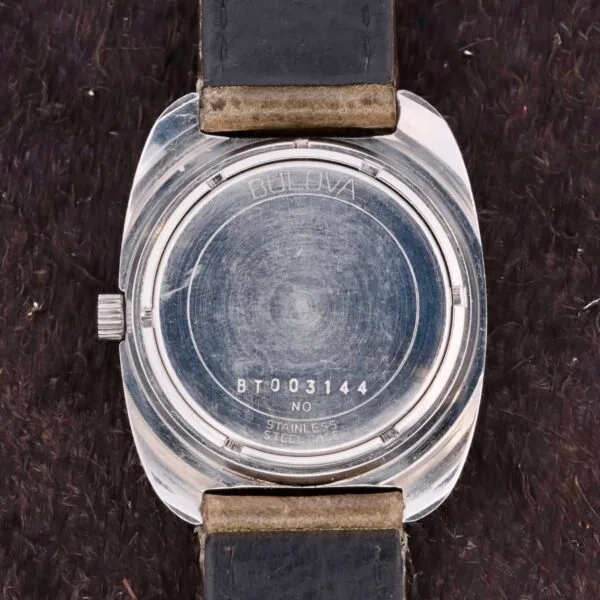 The back of a Bulova Sea King Blue Cross Hair Dial watch features a silver case and black leather strap. Engraved with Bulova BT003144, No, Stainless Steel, N4, it rests elegantly on a dark textured surface.