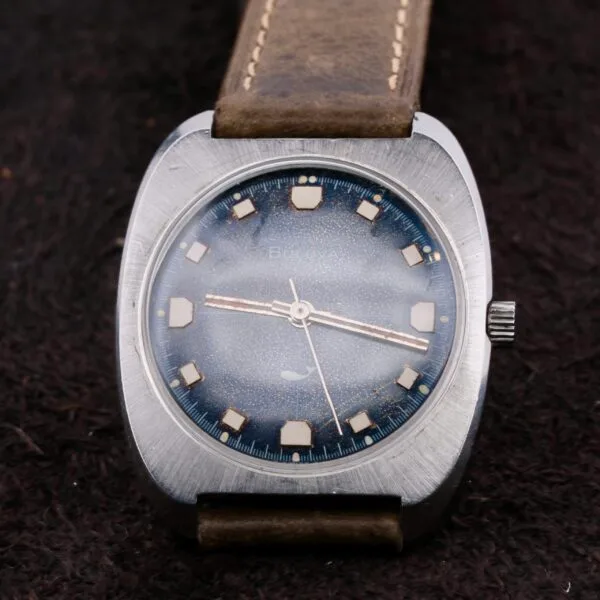 The Bulova Sea King Blue Cross Hair Dial Watch exudes vintage charm with a dark blue textured dial, silver indices, and a brown leather strap. Its stainless steel case adds to the classic look, creating a timeless piece.