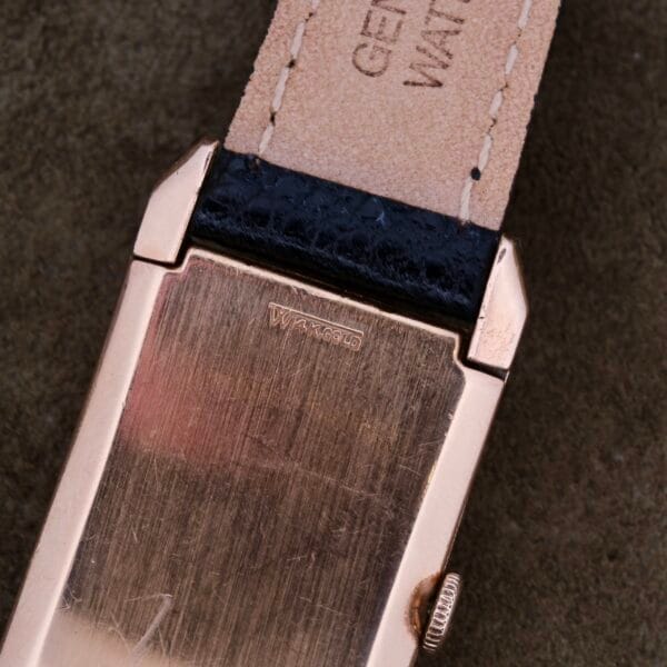 Close-up of a Gruen Curvex Salmon Dial 14k Rose Gold watch back, featuring WARRANTED on the case. The beige leather strap displays GENUINE LEATHER, highlighting its craftsmanship.