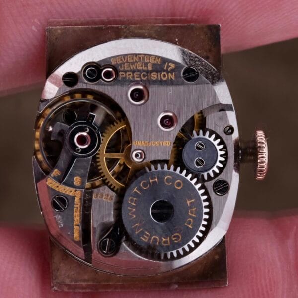 Close-up of a vintage watch movement with visible gears and intricate mechanisms, engraved with Seventeen Jewel 17 Precision and Gruen Watch Co. This detailed view is from the Gruen Curvex Salmon Dial 14k Rose Gold, highlighting its timeless charm.