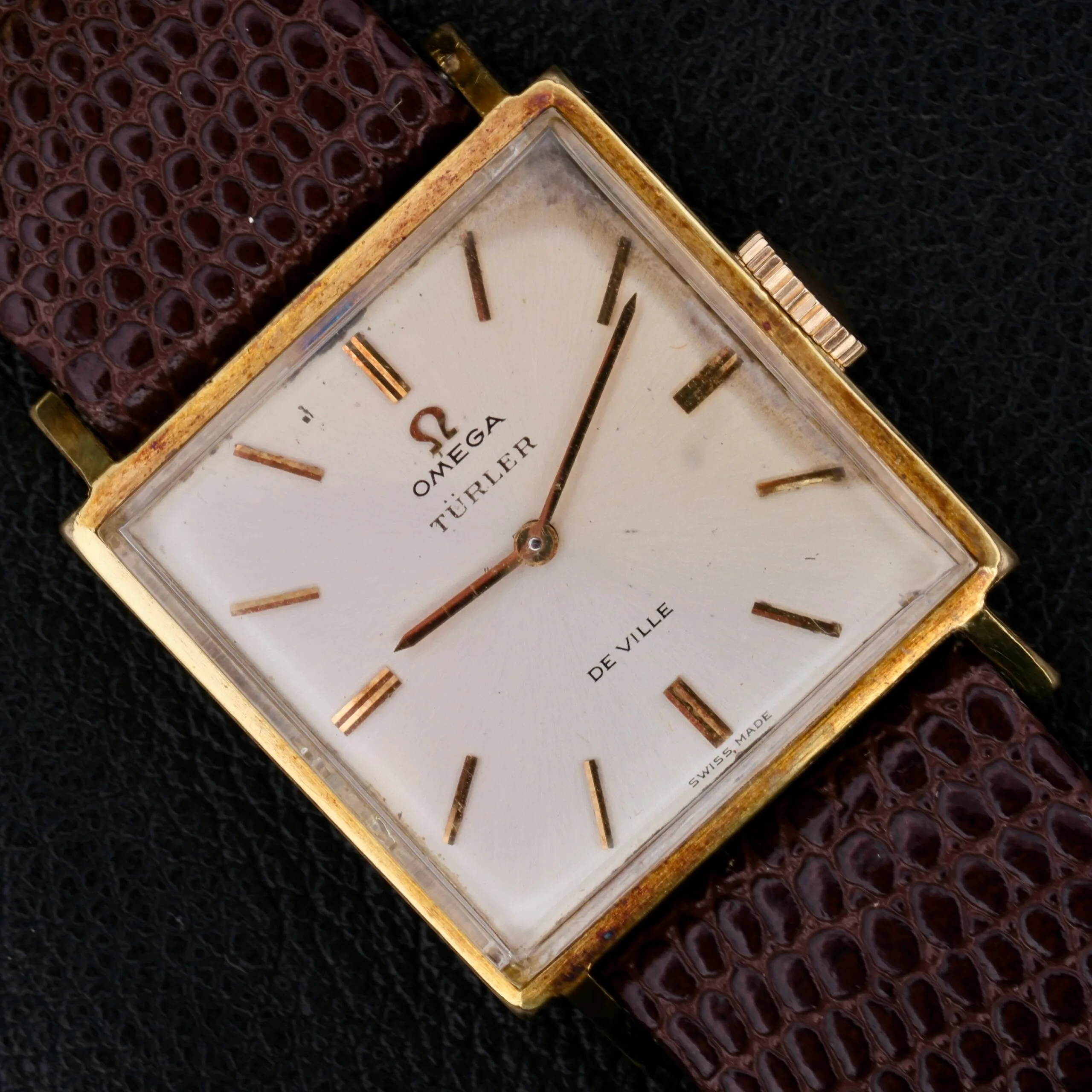 Omega Deville Turler Dial Square Case wristwatch featuring a gold case, white dial, and brown leather strap, shown on a black background.