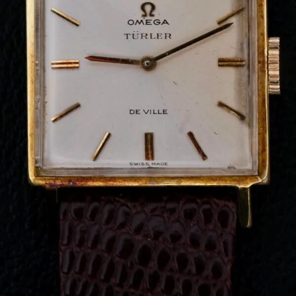 The Omega Deville Turler Dial Square Case watch showcases a vintage square gold design with a unique Türler dial and minimalist gold hour markers. Its textured brown leather strap adds elegance, and Swiss Made is inscribed at the bottom.