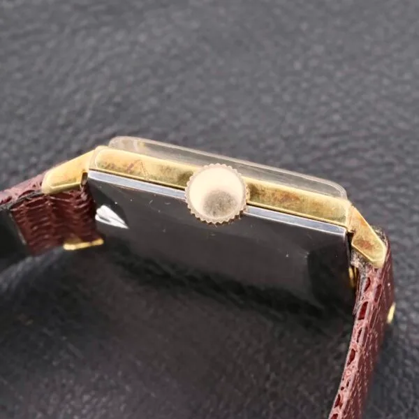 Close-up of an Omega Deville Turler Dial Square Case wristwatch with a brown leather strap. The gold-toned winding crown and angular case contrast against a textured dark background, showcasing the elegant side profile of the timepiece.