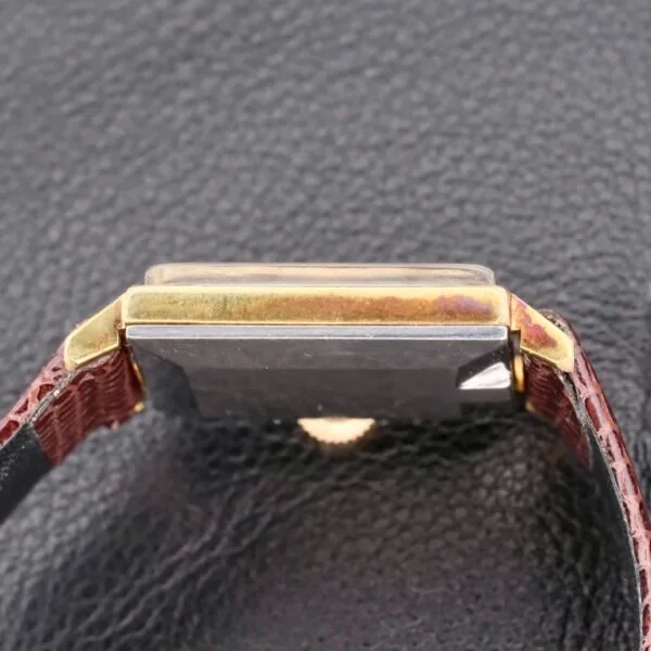 The Omega Deville Turler Dial Square Case wristwatch, featuring a rectangular face, gold edges, and a dark strap, rests face down on a textured black surface.