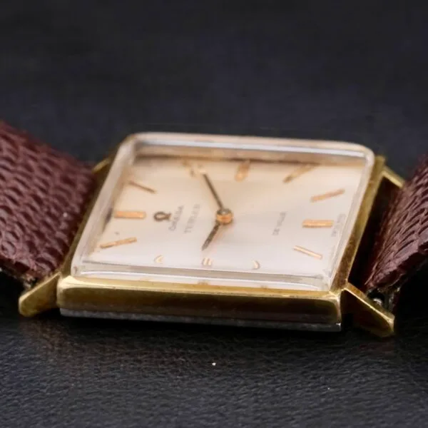 The Omega Deville Turler Dial Square Case wristwatch features a square gold case and a brown leather strap. Its cream dial with gold hour markers and hands adds timeless elegance.