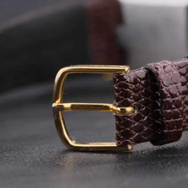 A close-up of a brown textured leather strap with a gold buckle rests on a dark surface. The Omega Deville Turler Dial Square Case enhances its artisan craftsmanship, accentuating its refined allure.