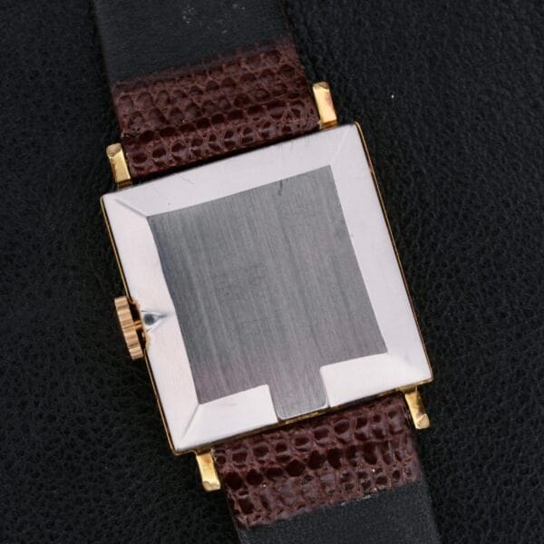 An Omega Deville Turler Dial square metal case wristwatch with a textured brown leather strap is elegantly displayed on a dark leather surface. The brushed-finish case back and gold-colored crown enhance the watchs refined craftsmanship.