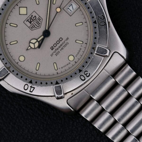 Close-up of a Tag Heuer Professional 2000 Dive watch with a silver bracelet, cream dial, date window at 3 oclock, and time measurement markings including an interval-marked rotating bezel.