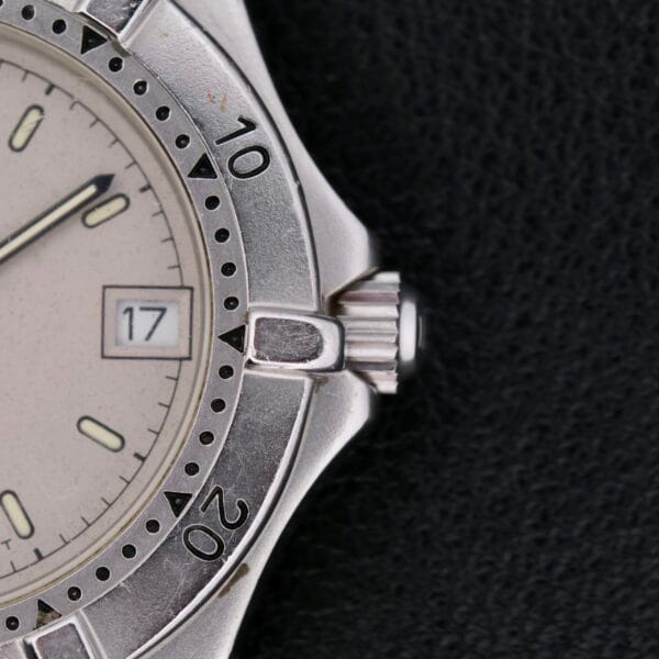 Close-up of a Tag Heuer Professional 2000 Dive watch with a silver analog design, white face, and date display showing 17. The hands point to about 10:10. The bezel features numbers at intervals against a black background.