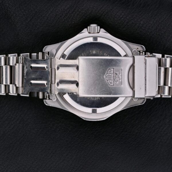 The image highlights the back of a silver metal wristwatch, identified as the Tag Heuer Professional 2000 Dive. It features an engraved logo and text on the case back, with a linked bracelet and clasp, elegantly presented on a black leather surface.