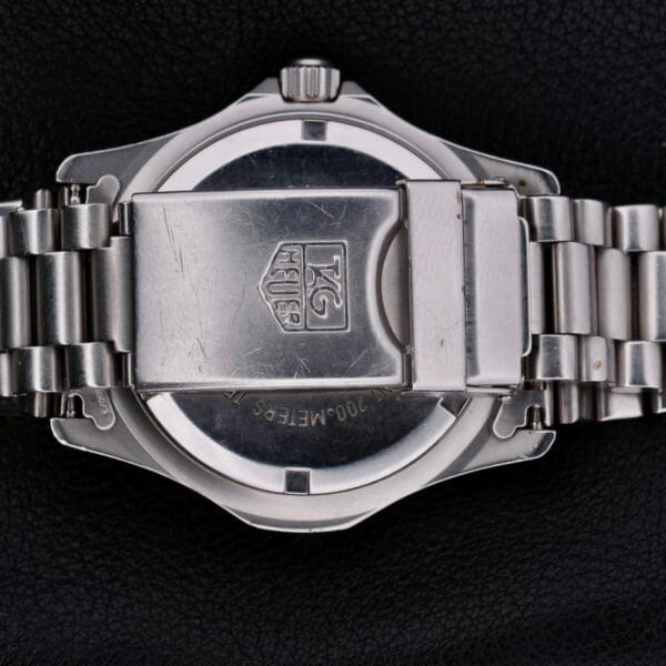 A close-up of the Tag Heuer Professional 2000 Dive wristwatch highlights a silver metal bracelet and clasp displaying the TAG Heuer logo on the back, elegantly set against a textured black background.