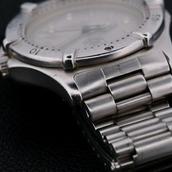 Close-up of a Tag Heuer Professional 2000 Dive with a silver metal link band. The watch face is slightly blurred but visible, displaying classic hour and minute hands. The bezel has marked indicators, and the metal surface shows subtle signs of wear.