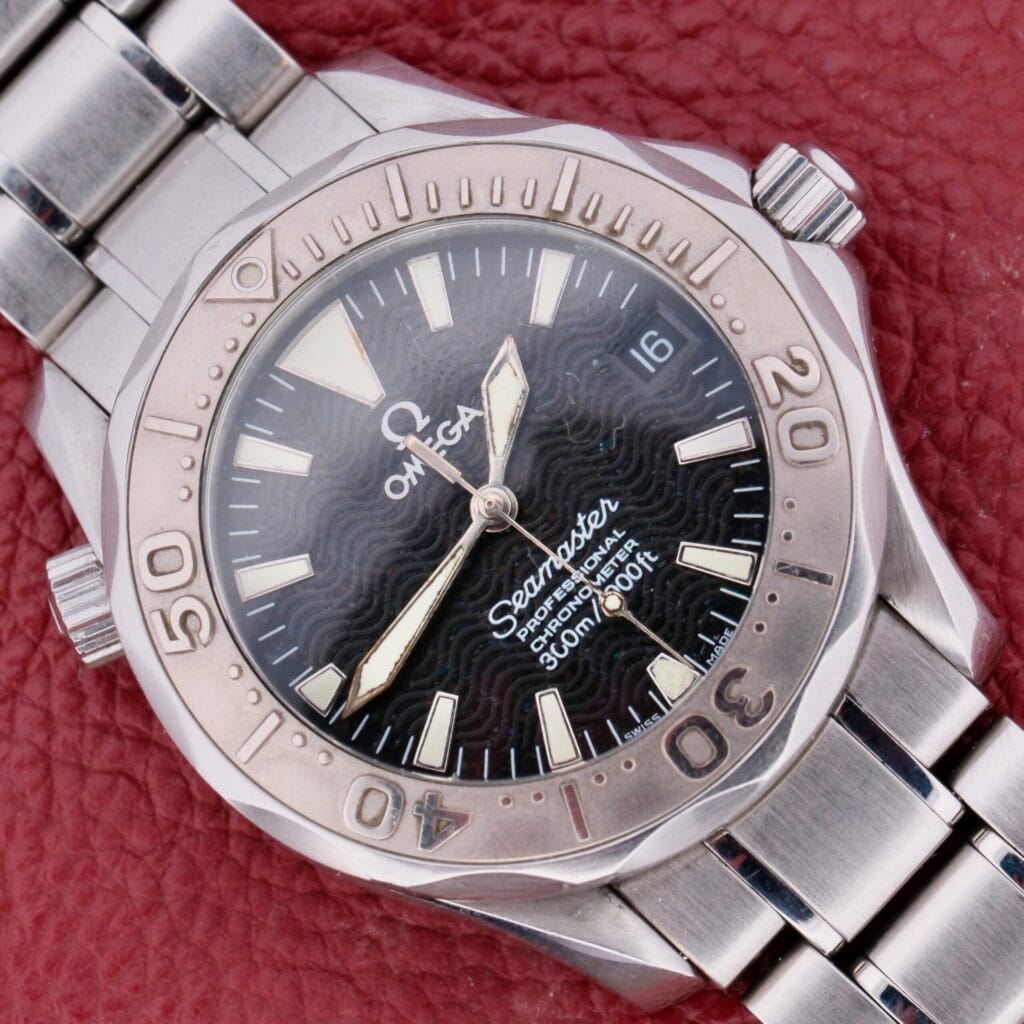 The Omega Seamaster Professional Chronometer features a silver case, black wavy dial, and metal band, displayed on red textured leather.