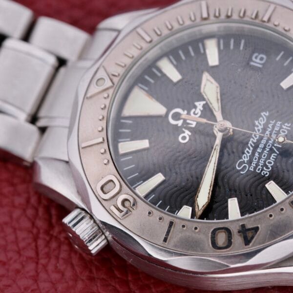 An Omega Seamaster Professional Chronometer watch with a metal band rests on a textured red surface. It has a silver bezel with numerals, a wavy black dial featuring luminous indices and hands, and includes a date display at the 3 oclock position.