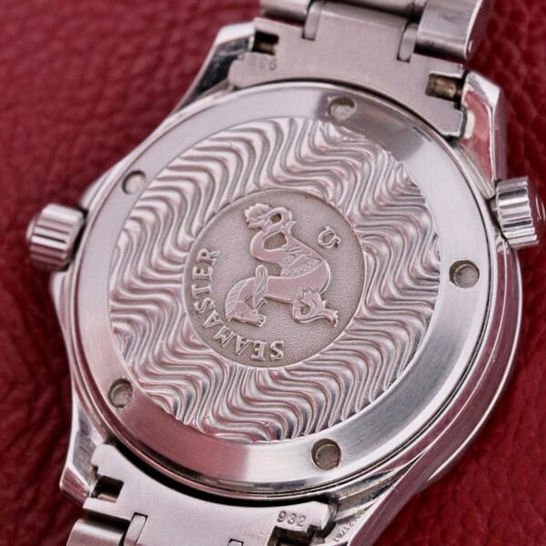 Close-up of the Omega Seamaster Professional Chronometers silver watch back, showcasing an engraved wave pattern and Seamaster with a detailed emblem, elegantly set against a textured red surface.