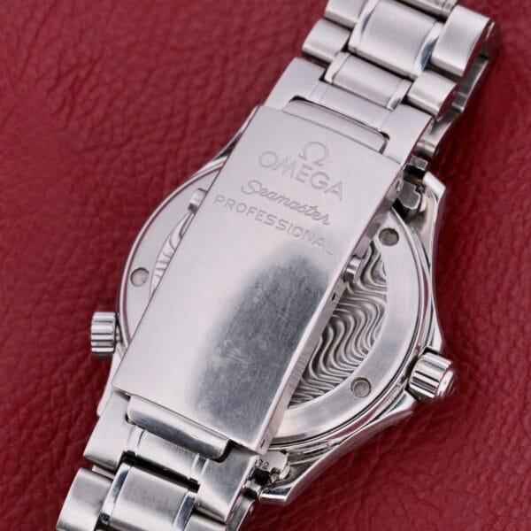 A close-up of the Omega Seamaster Professional Chronometer showcases its silver exterior, engraved clasp, and partially visible wave pattern on a red textured surface.