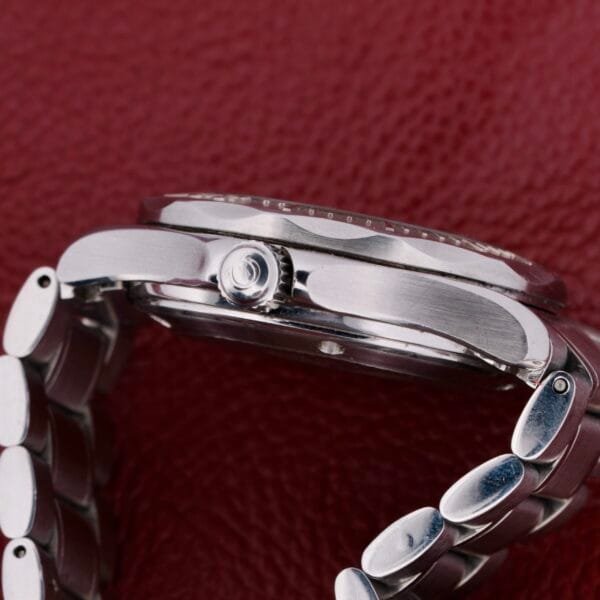A close-up of the Omega Seamaster Professional Chronometer on its side against a red textured background, highlighting the watchs side and metal link bracelet.
