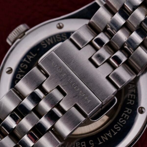 Close-up of a Hamilton American Classic Spirit Of Liberty stainless steel wristwatch with a metal link bracelet engraved Hamilton on the clasp. The Swiss-made watch faces back indicates its water-resistant.