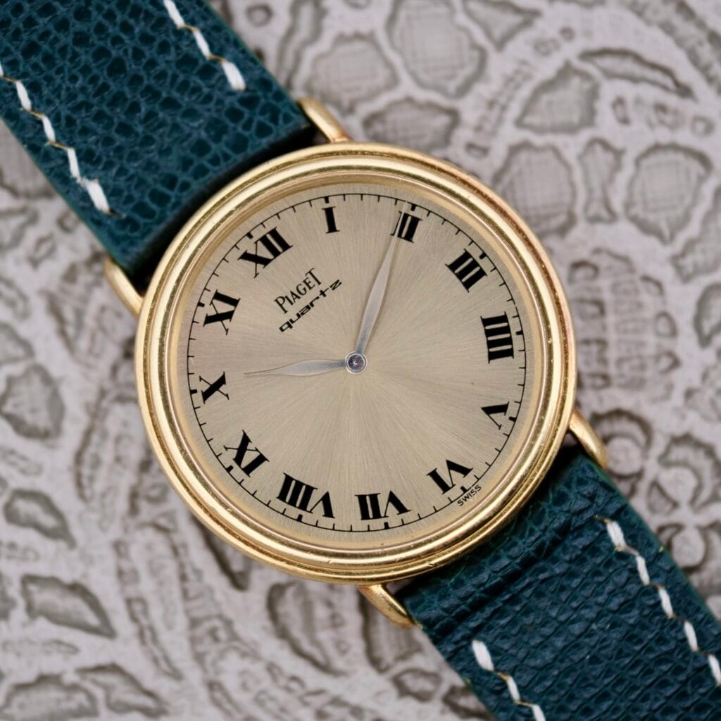 Piaget Quartz 7632 18k Gold watch with a champagne dial, Roman numerals, and a dark green leather strap displayed on a patterned background.