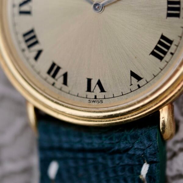 Close-up of a Piaget Quartz 7632 18k Gold Champagne Dial watch, showcasing a gold case with black Roman numerals on a beige face set to approximately 10:09. It features a dark textured leather strap with visible stitching and SWISS elegantly marked at the bottom.