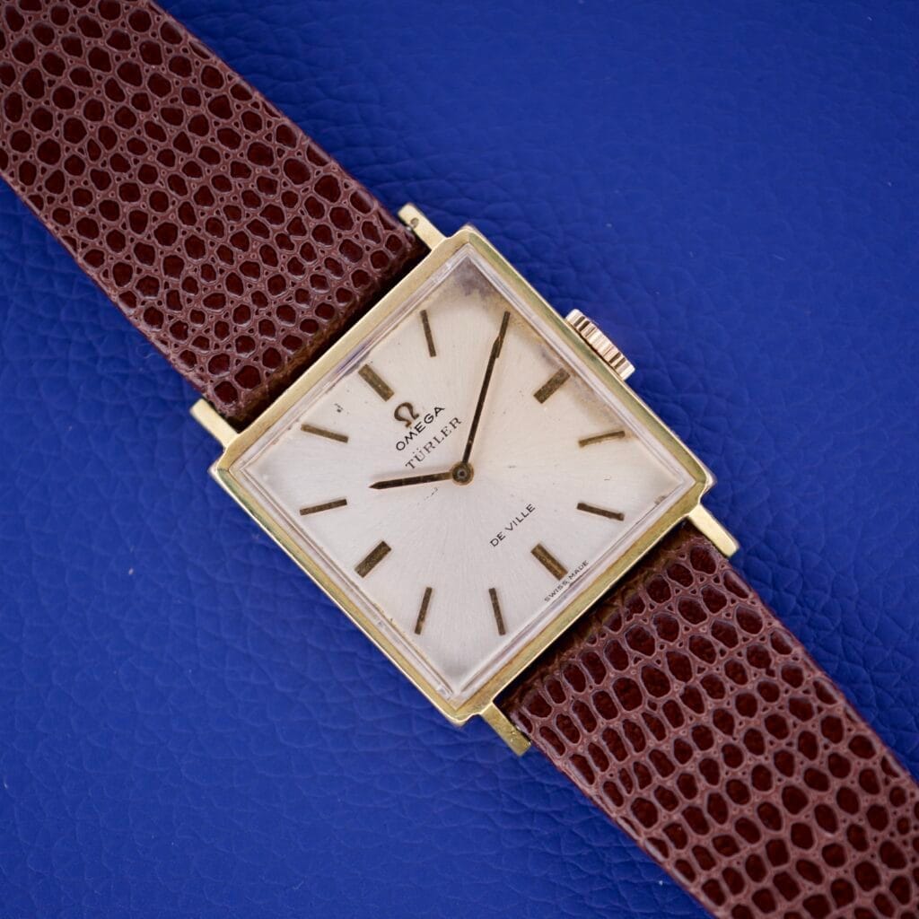 Omega Deville 111.071 Turler Dial Square Case wristwatch with a brown leather strap, displayed on a blue textured background.