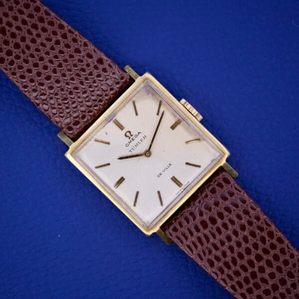 Omega Deville 111.071 watch with Turler Dial, square case, and brown leather strap shown on a blue background.