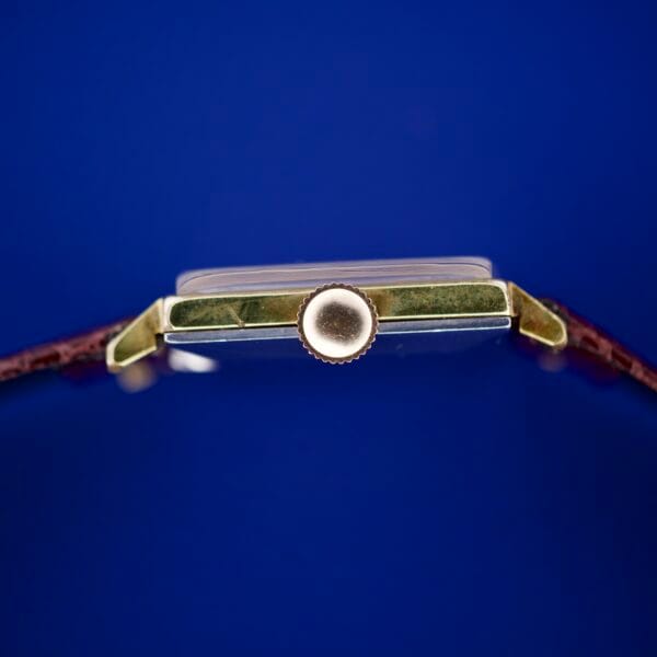 Side view of the Omega Deville 111.071 Turler Dial Square Case wristwatch featuring a gold crown and brown leather strap, set against a blue background.