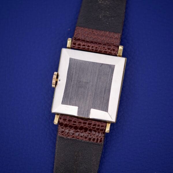 An Omega Deville 111.071 Turler Dial Square Case wristwatch with a brown and black leather strap is displayed on a blue textured background.