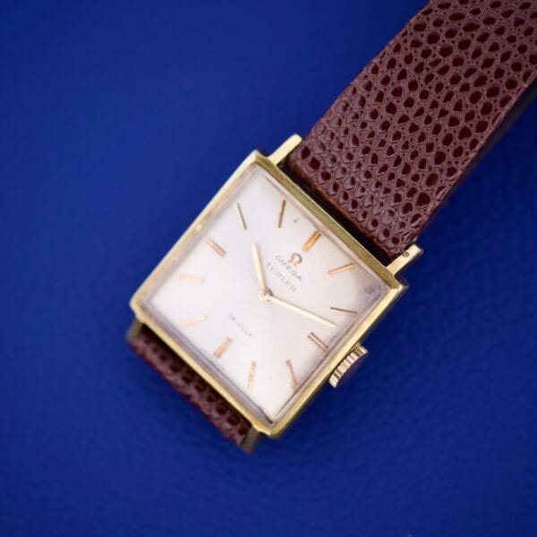 Omega Deville 111.071 Turler Dial Square Case wristwatch with a brown leather strap displayed on a blue surface.