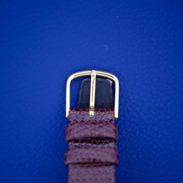 A brown leather watch strap with a gold buckle, ideal for the Omega Deville 111.071 Turler Dial Square Case, shown on a textured blue background.