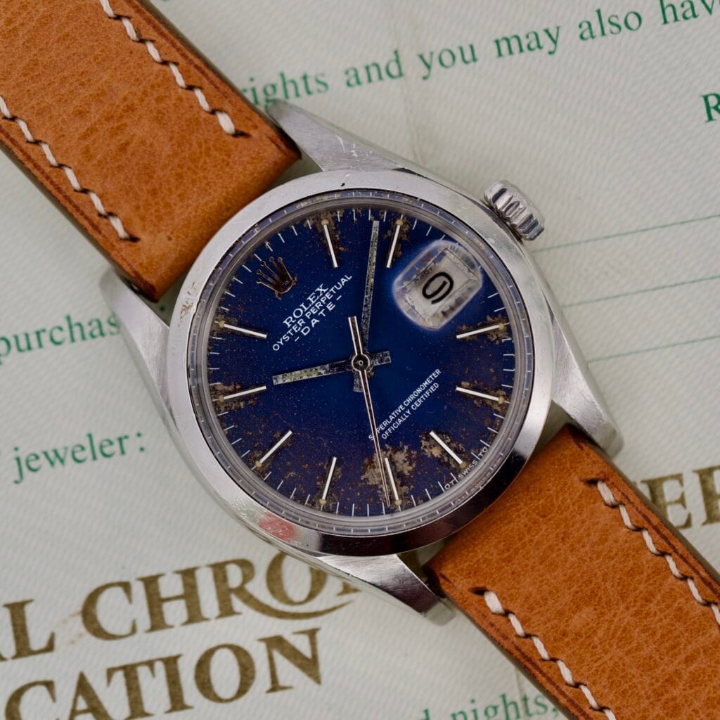 A Rolex Oyster Perpetual Date 1500 Blue Dial with a tan leather strap sits atop official documents.