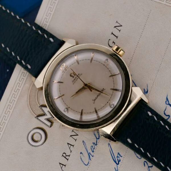 An Omega Seamaster Bull Horn Lug watch with a gold bezel and leather strap displays the time with elegance. The partially visible Omega logo on its certificate enhances its classic sophistication.