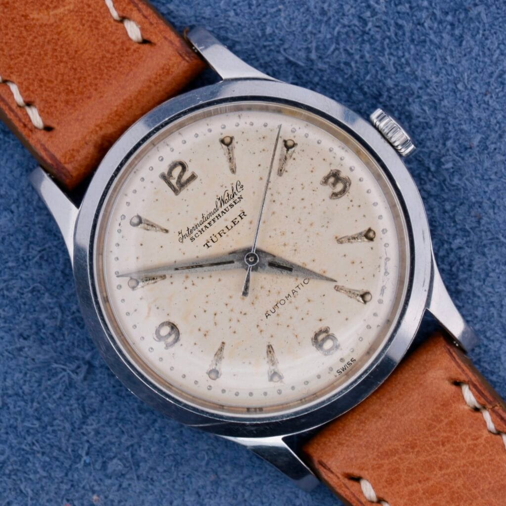 An IWC Automatic Turler Dial C. 852 wristwatch with a brown leather strap is displayed on a blue fabric background.