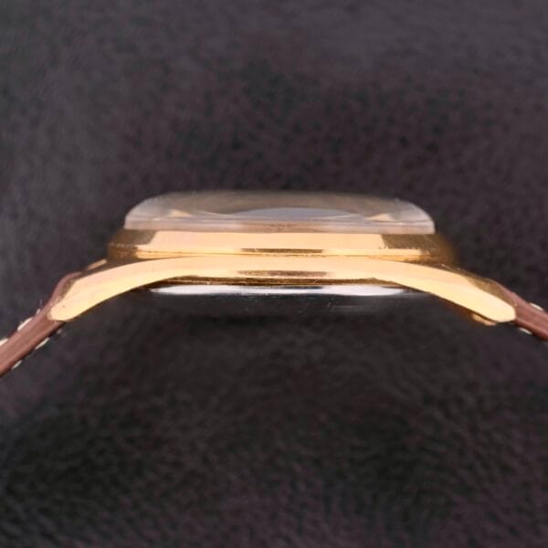 Side view of a Vulcain Cricket 17 Jewels watch face, featuring a gold-toned case and textured black background.