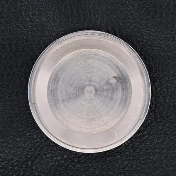A close-up of a round, transparent object with visible texturing resembling the intricate detailing of the Vulcain Cricket 17 Jewels, featuring a small bump on its surface against a black, textured background.