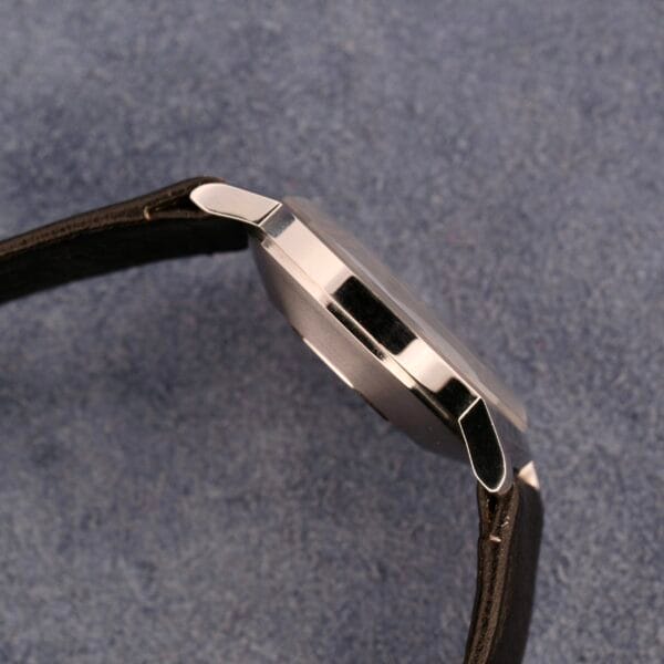 Side view of a Movado Sub-Sea Tempomatic Date wristwatch with a stainless steel case and black leather strap on a blue surface, highlighting its sleek design without showing the watchs face.