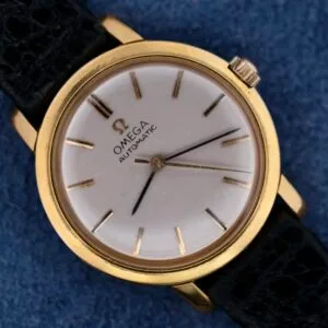 A close-up of the Omega Automatic Ladies wristwatch showcases its gold case, white dial, and black leather strap. It features elegant gold hour markers and hands on a striking blue textured background.