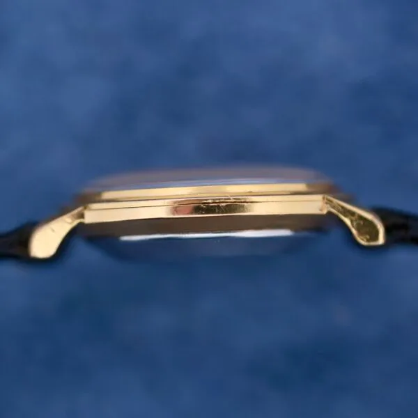 Close-up of the Omega Automatic Ladies wristwatch with a gold slim profile and black strap against a soft blue background.