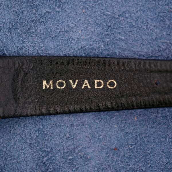 A close-up of a black leather strap with MOVADO embossed in silver letters, set against a textured blue surface, highlights the elegance of the Movado Sub-Sea Tempomatic Date collection.
