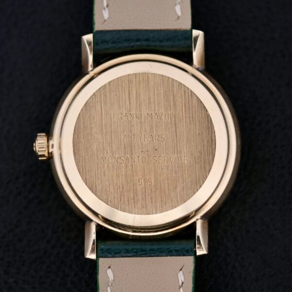 The Omega Automatic Day/Date Linen M Dial wristwatch features an inscription on the back reading FRANK MAZUT, 25 YEARS, MONSANTO SERVICE, 1979. It has a leather strap with white stitching and showcases a day/date display against a dark background.