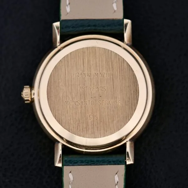 The Omega Automatic Day/Date Linen M Dial wristwatch features an inscription on the back reading FRANK MAZUT, 25 YEARS, MONSANTO SERVICE, 1979. It has a leather strap with white stitching and showcases a day/date display against a dark background.