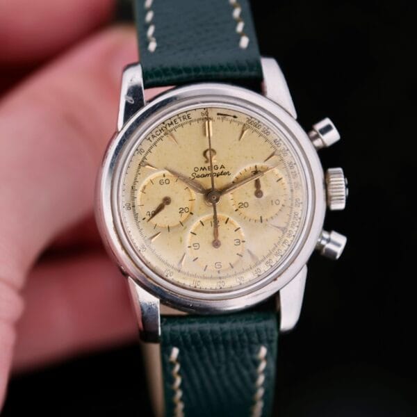 The Omega Seamaster Chronograph KO 2907 wristwatch features a cream dial with black numerals, three sub-dials, and a silver case paired with a green leather strap.