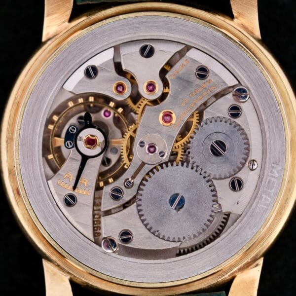 Close-up of the IWC Calatrava Jumbo 18ks mechanical movement, revealing its gold casing with visible gears, screws, cogwheels, and jewels that highlight the intricate inner workings.