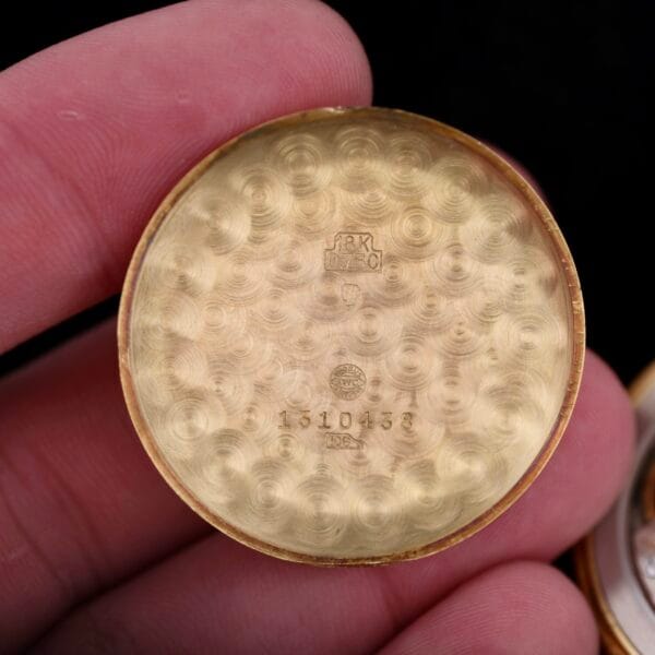 Close-up of an open watch case back being held, showing textured gold with markings 18K and 1310438, reminiscent of an IWC Caltrava Jumbo 18k design.