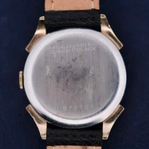 The image shows the back of a vintage Benrus Day/Date Pointer wristwatch with a metal case. Scratches reveal Stainless Steel Back and more markings. Its black band paired with a brown leather interior adds timeless elegance.