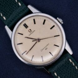 An Omega Seamaster 30 Ref 135.006 with a cream dial and green leather strap rests elegantly on a dark surface.