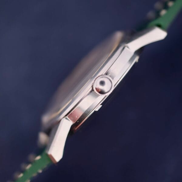 Close-up image of an Omega Seamaster 30 Caliber 286 with a metallic crown, minimalist design, sleek silver case, and green strap. Its details stand out beautifully against a blurred background.